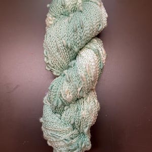 May include: A skein of light blue and white yarn with a textured, bumpy surface. The yarn is twisted into a figure eight shape.