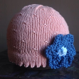 May include: A pink knitted hat with a blue crocheted flower on the side.