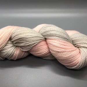 May include: A skein of yarn in a light pink and gray colorway. The yarn is soft and fluffy, and it is perfect for knitting or crocheting.