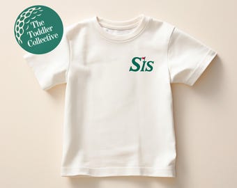 May include: White short-sleeved t-shirt with green text that says "Sis" and a small red flag above the "S".