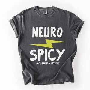May include: A dark gray t-shirt with a white lightning bolt and the text "Neuro Spicy" in white. The text "Inclusion Matters!" is printed in white below the graphic.