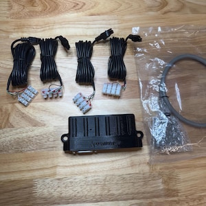 Könnte beinhalten: Ein schwarzes elektronisches Steuermodul mit dem Text "AutoMotion" und mehrere schwarze Kabelbündel mit Steckern. Ein graues Kabel befindet sich in einer transparenten Plastiktüte.