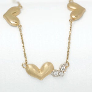 Peut inclure: Un collier en chaîne dorée avec trois pendentifs en forme de cœur et trois petits accents de diamants.