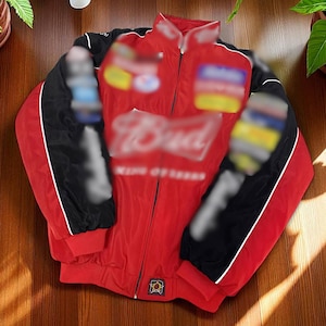 Puede incluir: Chaqueta de carreras roja con mangas negras y detalles blancos. La chaqueta tiene cierre de cremallera y logotipos borrosos, con la palabra "Bud" visible. Chaqueta deportiva, probablemente de material sintético.