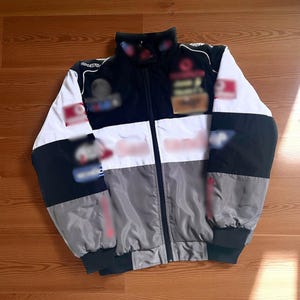 May include: A multi-colored jacket with a black, white, and gray design. The jacket has a zipper closure and a high collar. The sleeves are black and gray, and the body is white and gray. The jacket appears to be made of a lightweight material.