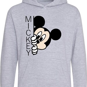 Puede incluir: Una sudadera con capucha gris con una imagen en blanco y negro de Mickey Mouse asom&aacute;ndose desde detr&aacute;s de la palabra "MICKEY".