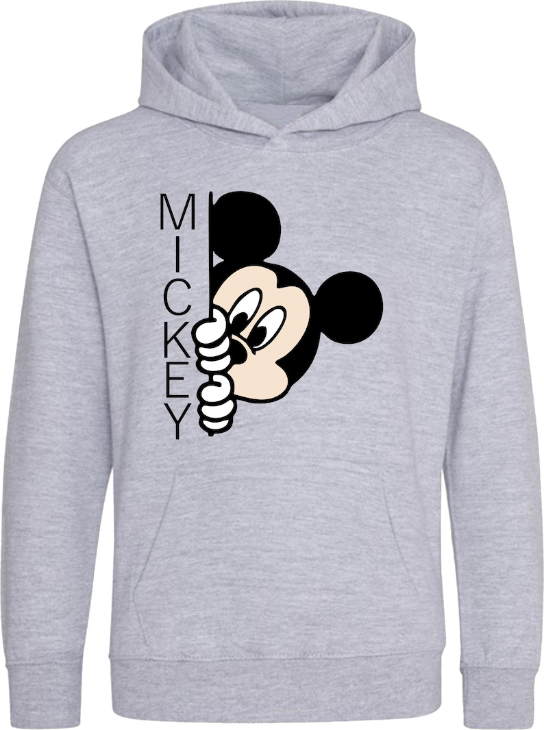 Puede incluir: Una sudadera con capucha gris con una imagen en blanco y negro de Mickey Mouse asom&aacute;ndose desde detr&aacute;s de la palabra "MICKEY".