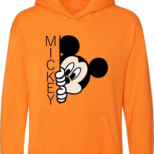 Puede incluir: Sudadera con capucha naranja con un gr&aacute;fico de Mickey Mouse en blanco y negro que asoma por detr&aacute;s de la palabra "MICKEY".