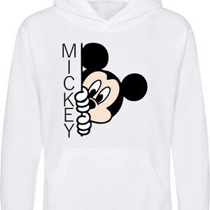 Puede incluir: Sudadera con capucha blanca con una ilustraci&oacute;n en blanco y negro de Mickey Mouse asom&aacute;ndose por la esquina. La palabra "MICKEY" est&aacute; impresa verticalmente en el lado izquierdo de la imagen.