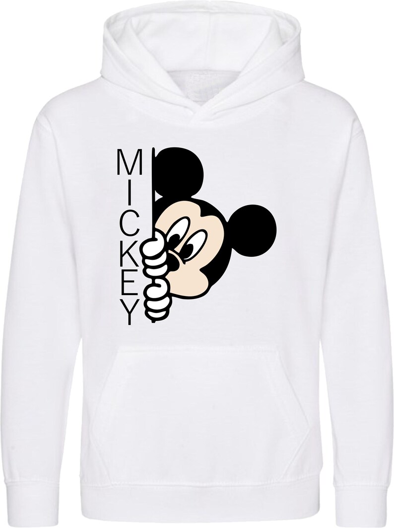 Puede incluir: Sudadera con capucha blanca con una ilustraci&oacute;n en blanco y negro de Mickey Mouse asom&aacute;ndose por la esquina. La palabra "MICKEY" est&aacute; impresa verticalmente en el lado izquierdo de la imagen.