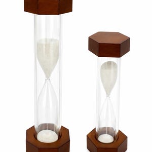 May include: Two hourglasses with dark brown wooden hexagonal bases and tops. Each hourglass features a clear glass cylinder containing fine white sand. The taller hourglass is positioned on the left, while the shorter one stands on the right.