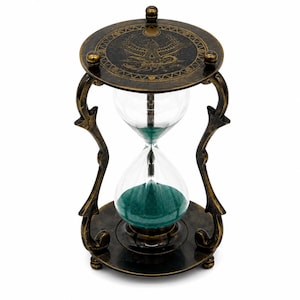 May include: An hourglass with a dark bronze-toned metal frame featuring ornate, curved supports. The top circular plate displays an engraved eagle emblem. The clear glass bulbs contain fine, vibrant green sand, currently flowing from the top to the bottom chamber.
