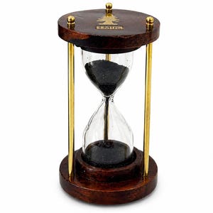 May include: A wooden hourglass with a dark brown base and top, connected by gold-colored metal rods. The hourglass contains black sand and is labeled "1 MIN". The top has a gold tree design.