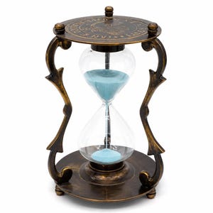 May include: An hourglass with a dark bronze-toned metal frame featuring curved supports and circular top and bottom plates. The top plate displays engraved text and a central graphic. Clear glass bulbs contain fine, light blue sand.