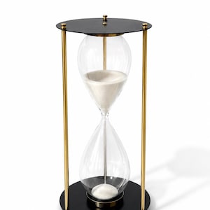 May include: An hourglass featuring a clear glass bulb filled with white sand, held within a frame consisting of two circular black metal plates connected by three vertical gold-toned metal rods, with small gold-toned decorative finials on top.