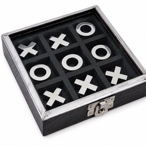 Op de afbeelding: Een vierkante boter-kaas-en-eieren spelset met een zwarte houten doos, een glazen deksel en een zilverkleurige metalen sluiting. Het binnenrooster bevat vijf zilverkleurige metalen X-stukken en vier zilverkleurige metalen O-stukken.