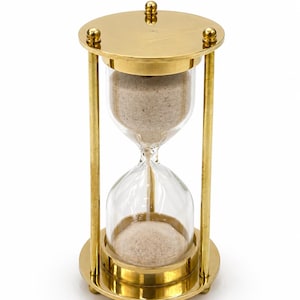 Könnte beinhalten: Eine Sanduhr aus Messing mit transparenten Glaskammern, die mit beigem Sand gefüllt sind. Die Sanduhr hat einen runden Sockel und eine runde Oberseite, die durch vier vertikale Messingstäbe verbunden sind. Ober- und Unterseite haben dekorative goldene Akzente.