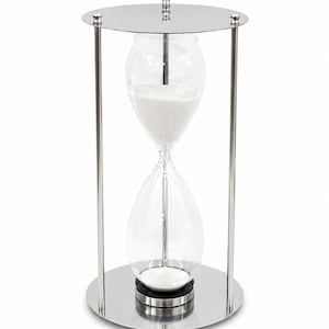 Pode incluir: Uma ampulheta alta com um bulbo de vidro transparente preenchido com areia branca, envolta numa estrutura de metal prateado polido com placas circulares superior e inferior suportadas por três hastes verticais finas e um remate central decorativo.