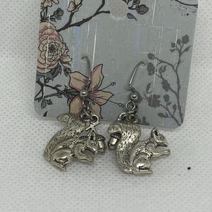 May include: Silver-colored squirrel earrings. Each earring features a detailed squirrel charm hanging from a silver-tone hook. The earrings are displayed on a floral-patterned card.