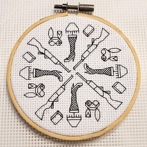 May include: A black and white embroidery hoop with a design of four stylized figures wearing boots and holding guns. The design is repeated four times around the hoop.
