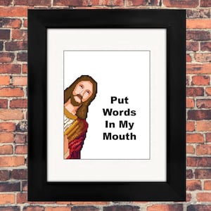 May include: A framed print with a black frame features a pixelated image of Jesus peeking from the left side. The text "Put Words In My Mouth" is displayed in black, bold font on a white background. The frame is set against a brick wall.