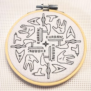 Könnte beinhalten: Ein weißer Stickrahmen mit schwarzem Garn, der ein Star Trek-Design darstellt. Das Design enthält das Star Trek-Logo, den vulkanischen Gruß und die Worte "Khaan!" mehrmals wiederholt.