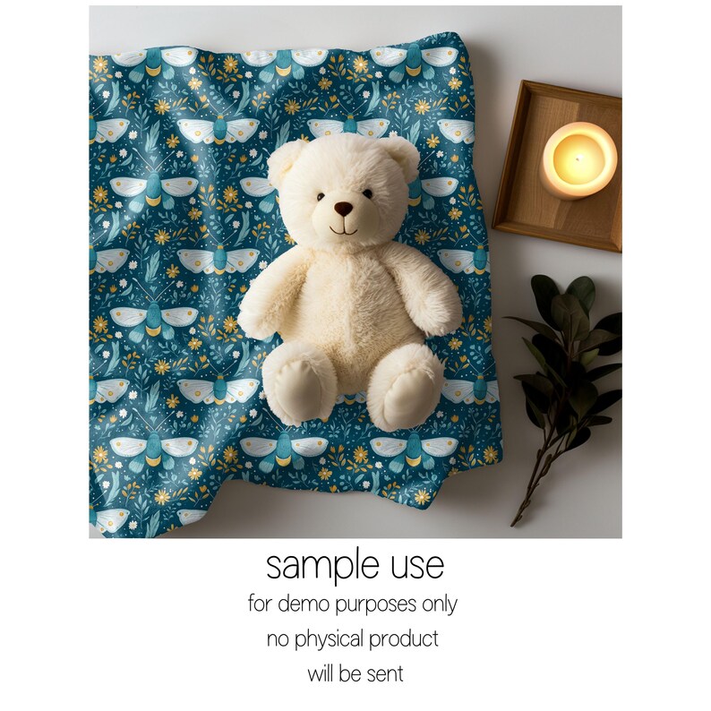 May include: A white teddy bear sitting on a teal blue fabric with a pattern of white moths and yellow flowers. The fabric is folded and the teddy bear is sitting in the center of the fabric.