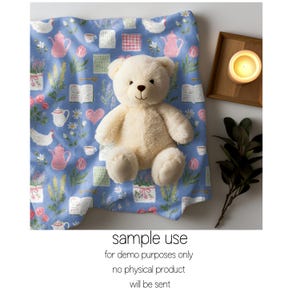 Pode incluir: Um urso de pel&uacute;cia creme est&aacute; sobre um cobertor azul com um padr&atilde;o floral e de bules rosa. O cobertor apresenta bules rosa, flores e livros abertos. Uma vela acesa numa bandeja de madeira e vegeta&ccedil;&atilde;o ao fundo. O texto "sample use" &eacute; vis&iacute;vel.