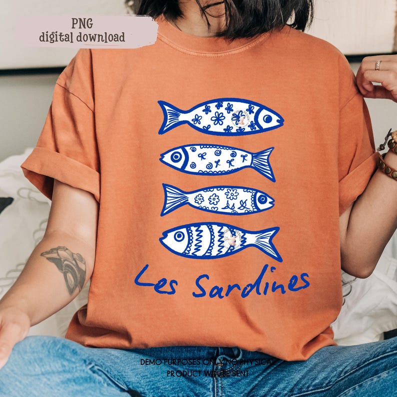 May include: Orange t-shirt featuring four blue fish illustrations with decorative patterns. The text "Les Sardines" is written in blue script below the fish. The top left corner of the image has the text "PNG digital download".