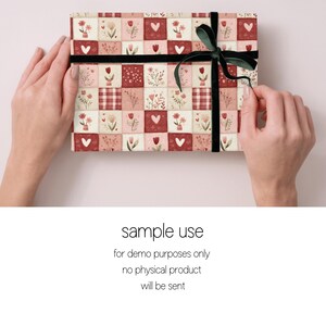 Peut inclure: Un coffret rectangulaire envelopp&eacute; dans du papier &agrave; motifs avec un motif floral et en forme de c&oelig;ur dans des tons de rouge, rose et cr&egrave;me. La bo&icirc;te est attach&eacute;e avec un ruban noir et un n&oelig;ud en velours vert. Le texte "sample use" est visible.