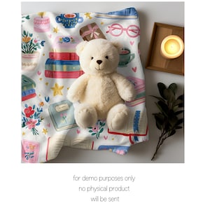 May include: A cream-colored teddy bear sits on a white blanket patterned with books, teacups, and flowers. A lit candle in a wooden tray and greenery are to the right. The blanket has a whimsical, storybook theme.
