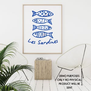 May include: A framed art print featuring four blue fish illustrations with decorative patterns. The text "Les Sardines" is written below the fish in blue script. The artwork is displayed in a bright, minimalist setting.