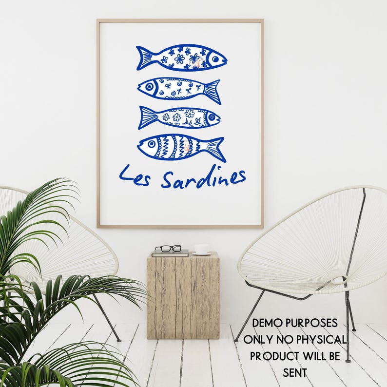 May include: A framed art print featuring four blue fish illustrations with decorative patterns. The text "Les Sardines" is written below the fish in blue script. The artwork is displayed in a bright, minimalist setting.