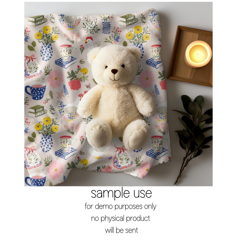 May include: A cream teddy bear rests on a floral blanket featuring vases, books, and teacups. The blanket has white, pink, yellow, and blue details. A lit candle in a wooden tray and greenery are also visible.