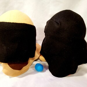 May include: Two plush toys, one with a tan head and black hat, the other with a black head and black hat. A blue ball is in front of the toys.