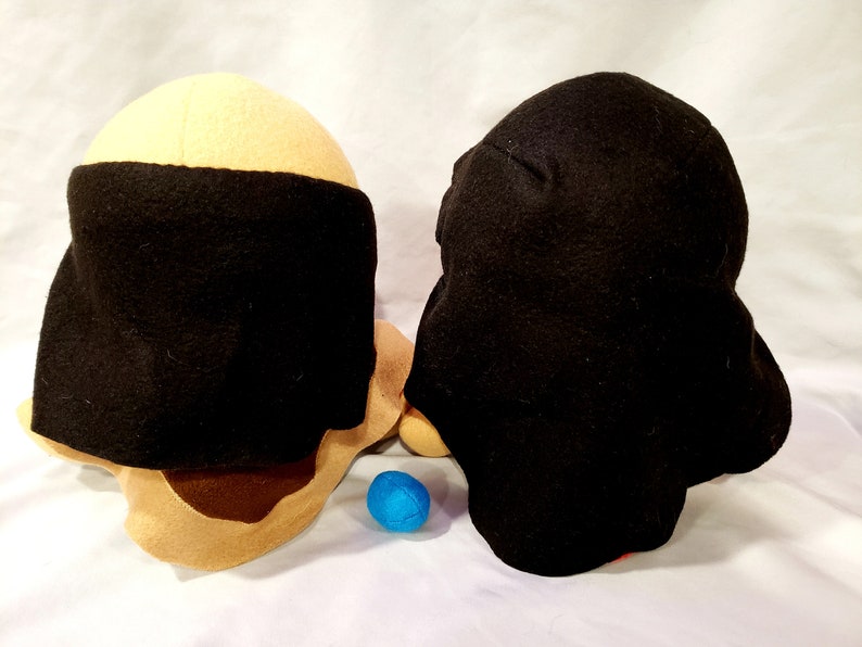 May include: Two plush toys, one with a tan head and black hat, the other with a black head and black hat. A blue ball is in front of the toys.