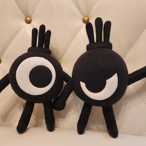Puede incluir: Dos juguetes de peluche negros con ojos y bocas blancas. Los juguetes tienen brazos y piernas largos y están de pie sobre una superficie blanca.