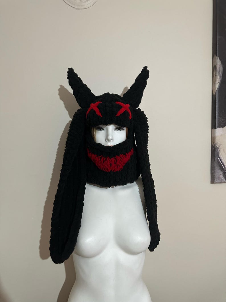 May include: Black knit bunny hat with long ears and a red stitched smile. The hat has red X's on the top.