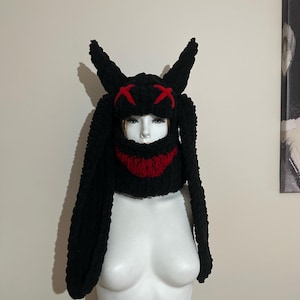 May include: Black knit bunny hat with long ears and a red stitched smile. The hat has red X's on the top.