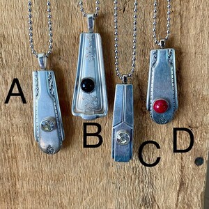 May include: Four silver necklaces with different colored stones on a wooden background. The necklaces are labeled A, B, C, and D.