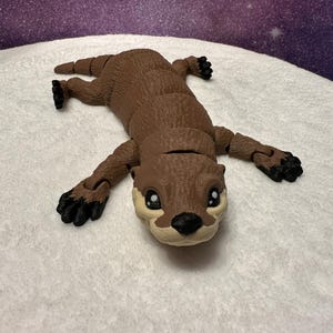 May include: A brown and black articulated otter toy with a segmented body. The toy has a realistic otter face with black eyes and a brown nose.