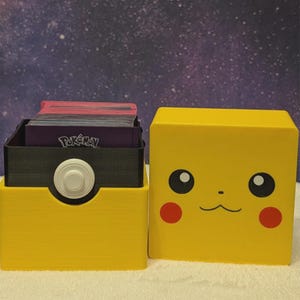 May include: A yellow storage box with a Pikachu face design next to a yellow and black card holder. The card holder has a white button and holds a stack of cards with the Pokémon logo.