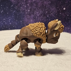 May include: A brown and tan articulated bison figurine with a furry texture. The figurine is standing on a white surface.