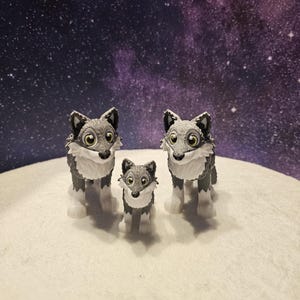 May include: Three gray and white wolf figurines with black eyes and noses. The figurines are standing on a white surface.