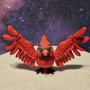 May include: A red cardinal figurine with outstretched wings. The bird has black accents on its face and feet. The figurine is set against a backdrop of a starry night sky.