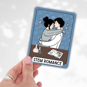 May include: A blue card with the text "STEM ROMANCE" features a cartoon illustration of two people embracing. The background has science-themed doodles. A hand holds the card.