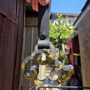 May include: A clear, cloud-shaped keychain with gold leaf accents and a black strap. The keychain has a black button and is held up by a black strap. The cloud shape has a swirling design.