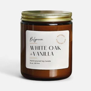 May include: A brown glass jar candle with a gold lid. The label reads "Belgreen. WHITE OAK + VANILLA" with "Hand-poured Soy Candle" and "8 oz | 65 hrs" below. A "NATURAL ECO FRIENDLY" seal is on the right.