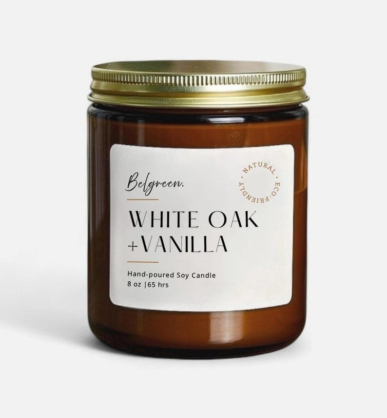 May include: A brown glass jar candle with a gold lid. The label reads "Belgreen. WHITE OAK + VANILLA" with "Hand-poured Soy Candle" and "8 oz | 65 hrs" below. A "NATURAL ECO FRIENDLY" seal is on the right.