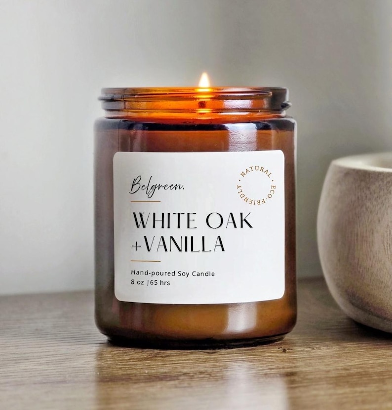 May include: A lit, hand-poured soy candle in a brown glass jar. The label reads "Belgreen. WHITE OAK + VANILLA" with "NATURAL ECO-FRIENDLY" text. The candle is 8 oz and has a 65-hour burn time.